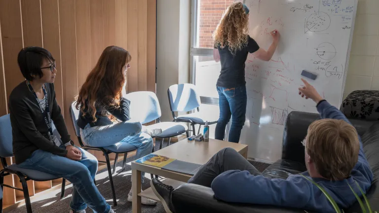 Group of students working together on scientific equations at a whiteboard.